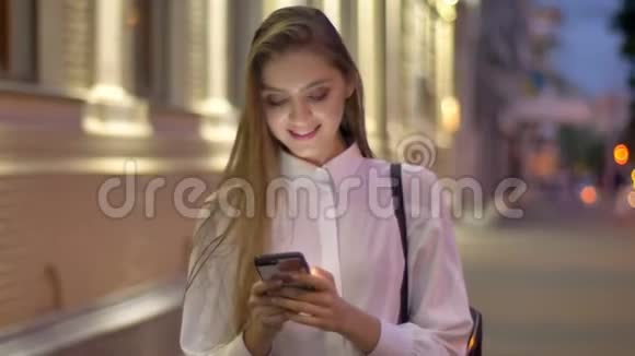 年轻迷人的女孩正在夏天的晚上在智能手机上输入信息笑着交流的概念视频的预览图