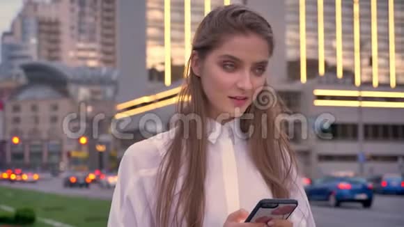 夏天在市中心的日落时分年轻可爱的女孩在看她的智能手机思考概念交流视频的预览图