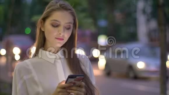 年轻漂亮的女孩在夏天的晚上在智能手机上输入信息触摸头发交流观念视频的预览图