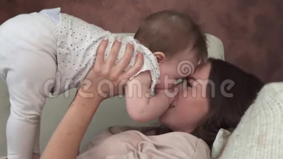 快乐的妈妈躺在沙发上微笑着亲吻可爱的宝宝视频的预览图