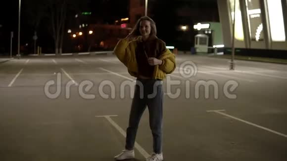 苗条穿着灰色裤子和黄色外套的精致女孩正在跳舞在外面的停车场上玩得很开心视频的预览图