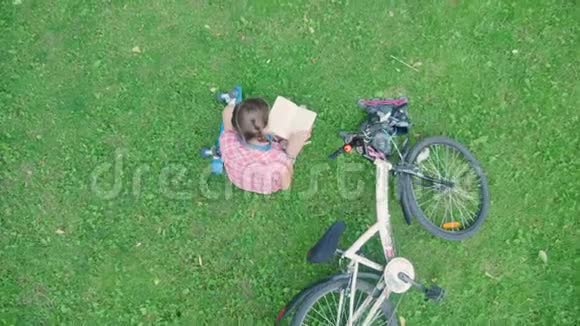 顶景可爱的女孩在公园里坐在草地上读一本好书视频的预览图