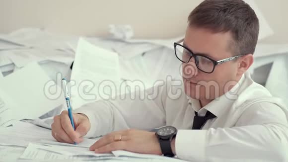 一个戴眼镜的疲惫的年轻人坐在一堆文件和签名文件里因为疲劳一个人心烦意乱视频的预览图