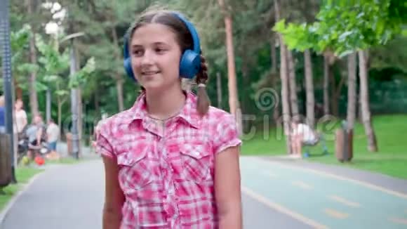美丽的少女在公园里听蓝耳机溜冰鞋的音乐视频的预览图