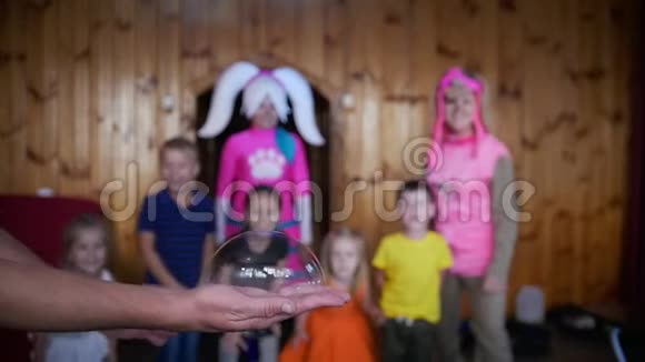 在前景中一个人手一个人在手上点燃一个肥皂泡背景是孩子们和崇拜者视频的预览图