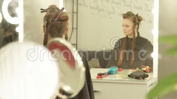 在美容工作室里坐在椅子前镜里的年轻女子用夹子固定长发妇女视频的预览图