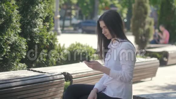 年轻女性白天坐在城市的长椅上使用智能手机视频的预览图