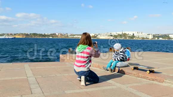 一个女孩在海边的智能手机上给一个孩子拍照视频的预览图