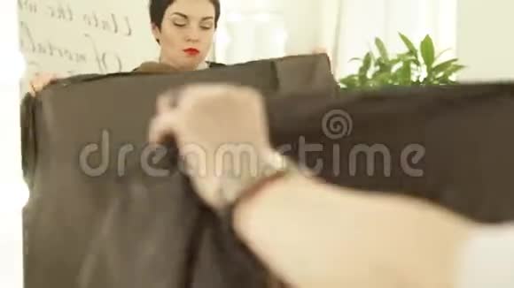 理发师在理发室理发前在年轻女子身上穿着斗篷长袍为理发做准备视频的预览图