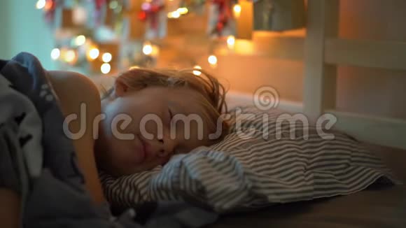 一个睡在床上的小男孩的慢镜头伴随着圣诞灯的灯光照亮了他的一个日历视频的预览图