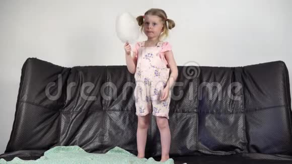 一个快乐的小女孩站在沙发上吃棉花糖视频的预览图