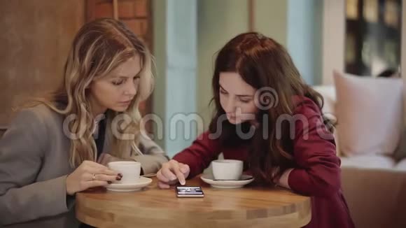 两个年轻有魅力的朋友在咖啡馆聊天打电话拍照片视频的预览图