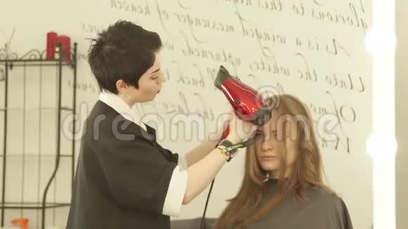 在美发沙龙里用吹风机和梳子给长发发型时有魅力的女人把剪发机烘干视频的预览图