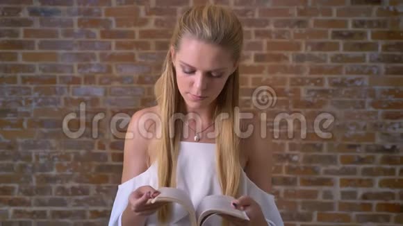 年轻的白种人金发女孩看书肖像砖墙的背景视频的预览图