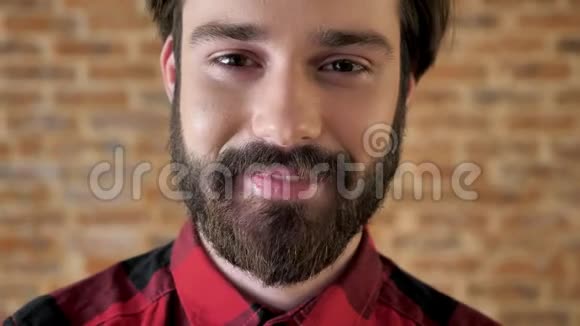年轻迷人的留着胡子的快乐男人正在笑在镜头前看着砖背景视频的预览图