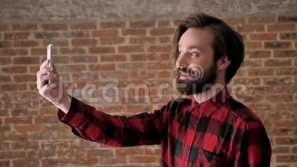 年轻有魅力的留着胡子的小伙子在网上智能手机上用视频聊天交流概念砖背景视频的预览图