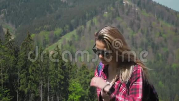 一个年轻的白种人女人带着背包和太阳镜上山调整风中的头发视频的预览图