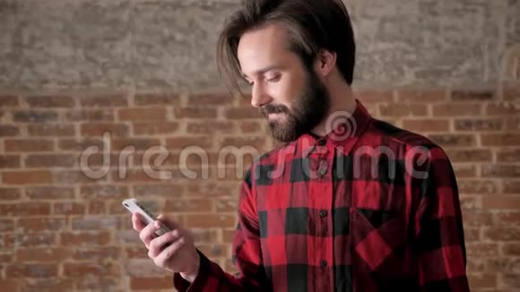有胡子的年轻帅哥在智能手机上看照片交流概念砖背景视频的预览图