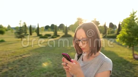 漂亮迷人的女孩在智能手机上和朋友聊天头发在夏风中飘扬视频的预览图