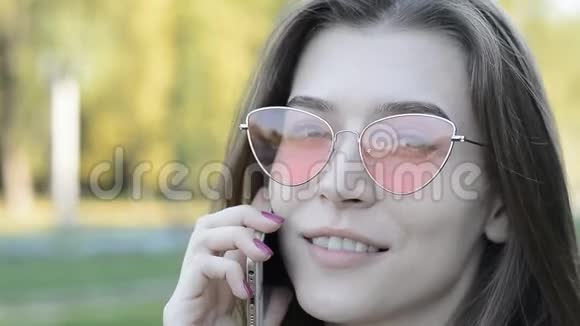 一位戴着粉红色太阳镜的年轻白种人美女在公园打电话的画像视频的预览图
