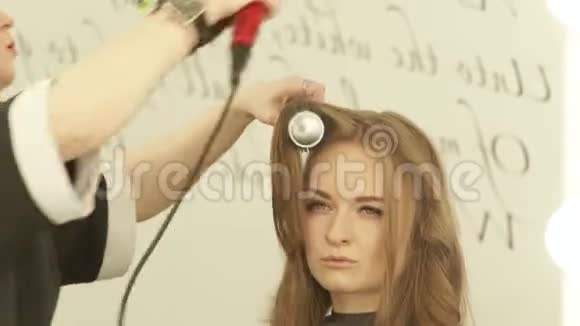 金发女人在理发店用吹风机和发刷给长发把剪发机烘干视频的预览图