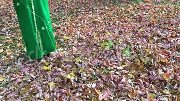 美丽快乐的女人穿着绿色的裙子在秋天的公园里收集树叶把它们扔起来视频的预览图