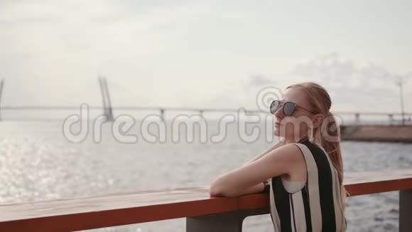 一个戴太阳镜的女人正在河堤休息假日概念4K视频的预览图