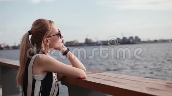 一个戴太阳镜的女人正在河堤休息假日概念4K视频的预览图