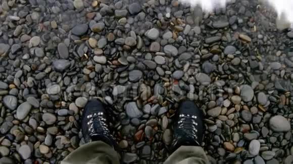 近景拍摄的是一片岩石海滩一名男子穿着靴子站在地面上海浪拍打着海岸视频的预览图