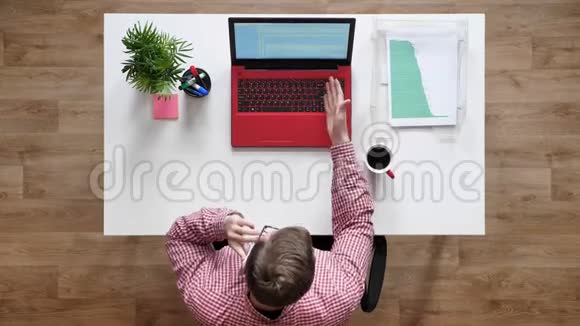 戴眼镜的年轻人打电话顶头坐在办公桌后面手提电脑咖啡和文件视频的预览图