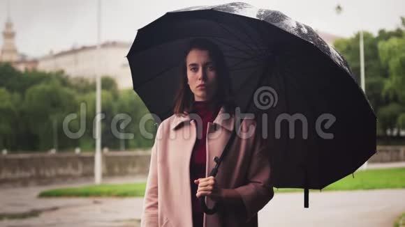 雨中站在伞下的年轻严肃的女人城市的悲伤天气视频的预览图