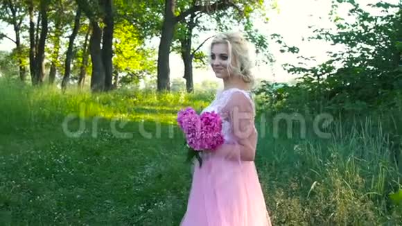 一幅美丽的金发女子手持一束粉红色玫瑰的户外画像视频的预览图