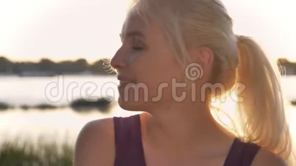 年轻的金发女人看镜头的肖像可爱的微笑阳光灿烂河流和自然的背景视频的预览图