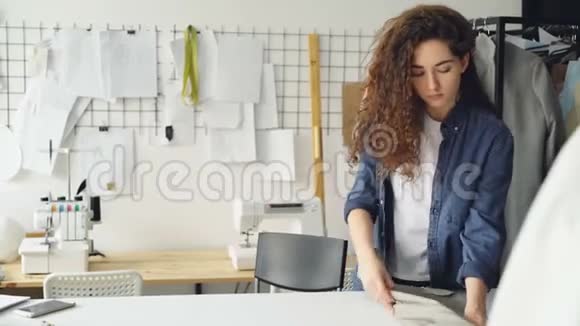女裁缝在工作室的桌子上滚动织物螺栓然后拍摄服装草图并在纸上画画设计视频的预览图