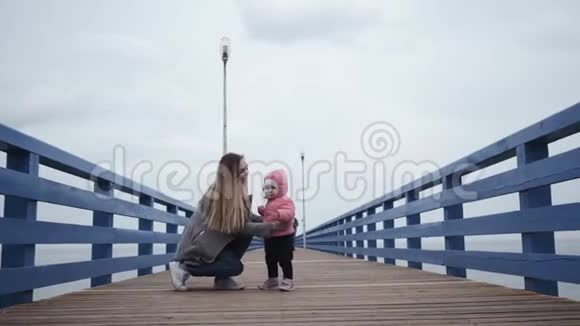 年轻快乐的女人妈妈和一个小女孩走在一起亲吻她的女儿沿着海滨长廊的第一步视频的预览图