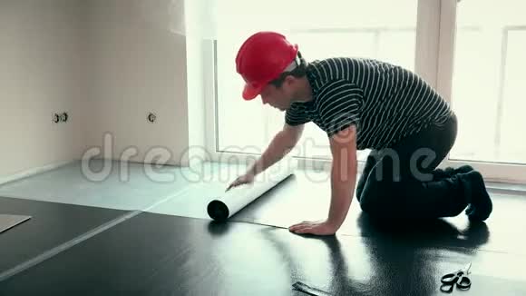 专业建筑工人戴红色头盔在新房间铺设垫垫视频的预览图