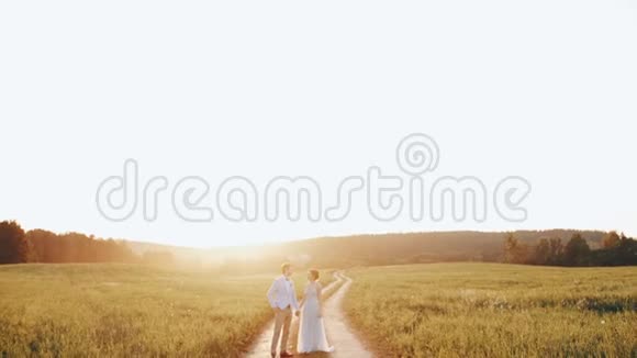 新娘和新郎站在夕阳下的乡间小路上手牵手视频的预览图