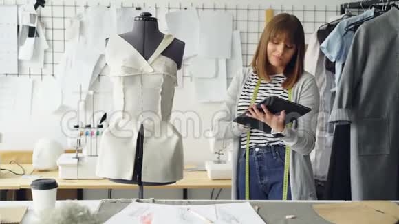 年轻的时装设计企业家正在使用平板电脑同时检查固定在裁剪假人上的服装现代视频的预览图
