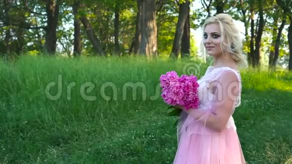 一幅美丽的金发女子的户外肖像手捧一束粉红色的花视频的预览图
