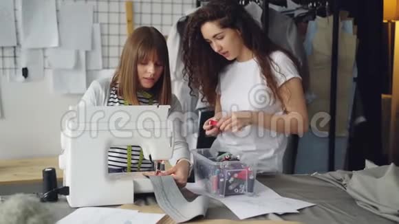 年轻女性的女设计师在缝纫机上工作而她的另一半则在看缝纫和缝纫线视频的预览图