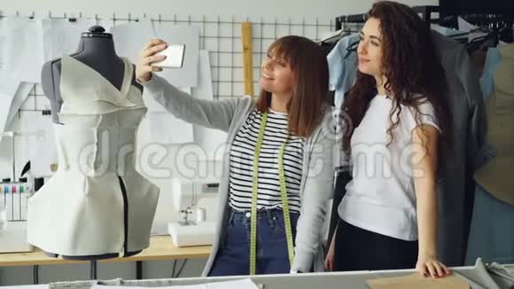 两位有创意的女设计师在工作场所站在裁缝旁边用智能手机自拍视频的预览图