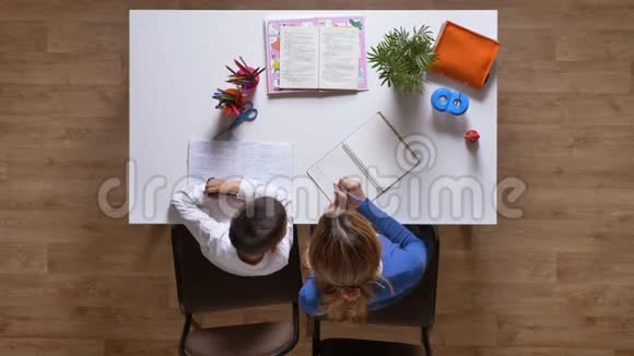 年轻的母亲帮助儿子学习坐在桌子后面孩子写作业顶着木地板射击视频的预览图