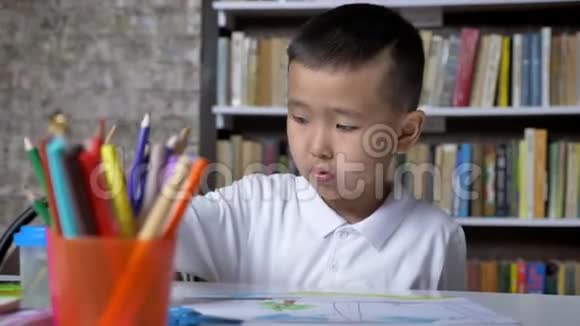 年轻的亚洲儿童集中在纸上坐在桌子后面男孩做作业书架背景视频的预览图
