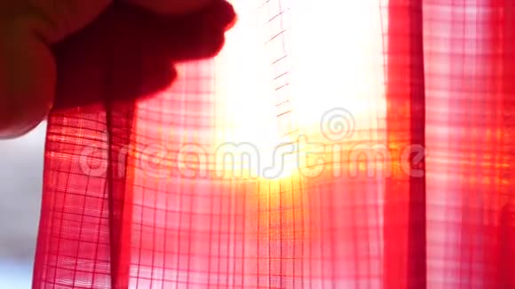 女孩摸着红色的窗帘用手在阳光的光线下玩耍双手合拢视频的预览图