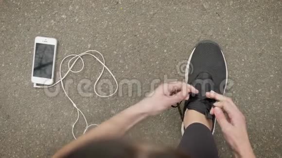 女运动员系着鞋带而她的智能手机和耳机则躺在地上通讯概念视频的预览图