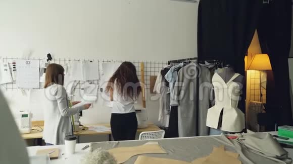年轻的企业家服装设计师站在墙前挂着草图讨论图纸和放置视频的预览图