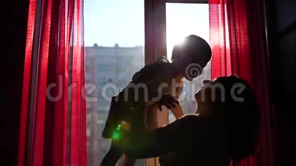 一位年轻而快乐的母亲正把她的孩子抱在窗户旁边太阳光线穿过窗户笑声视频的预览图