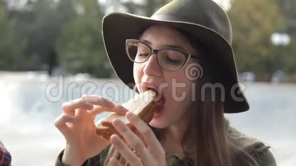一个戴着眼镜和帽子的年轻女孩正在尝试一个美味的三明治食物视频的预览图