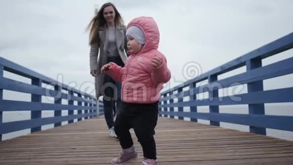 年轻快乐的女人妈妈和一个小女孩走在一起亲吻她的女儿沿着海滨长廊的第一步视频的预览图