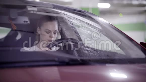 穿着白色衬衫的漂亮女孩坐在红色的车里手里拿着方向盘视频的预览图